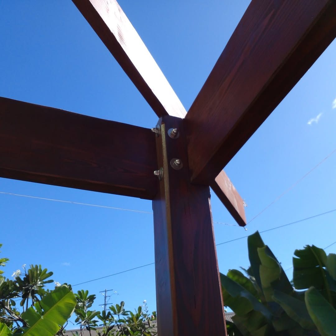 Assemblage de poutres de pergola boulonnées sur poteau, ciel bleu et bananiers